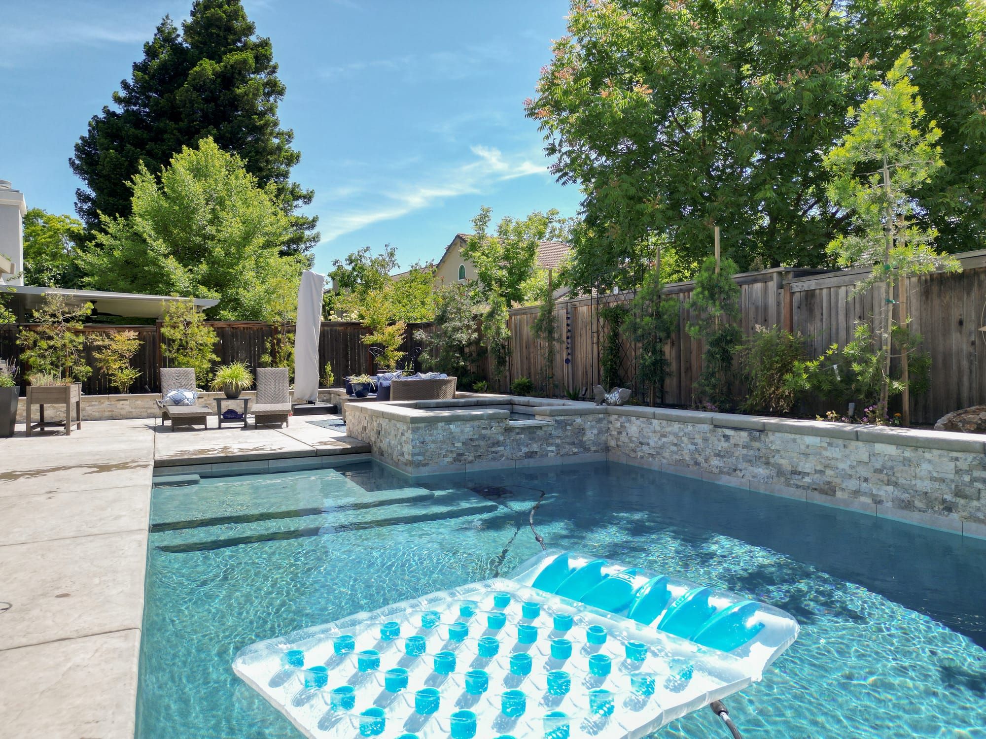 Backyard pool with stone veneer spa, patio seating, and mature landscaping in Sacramento