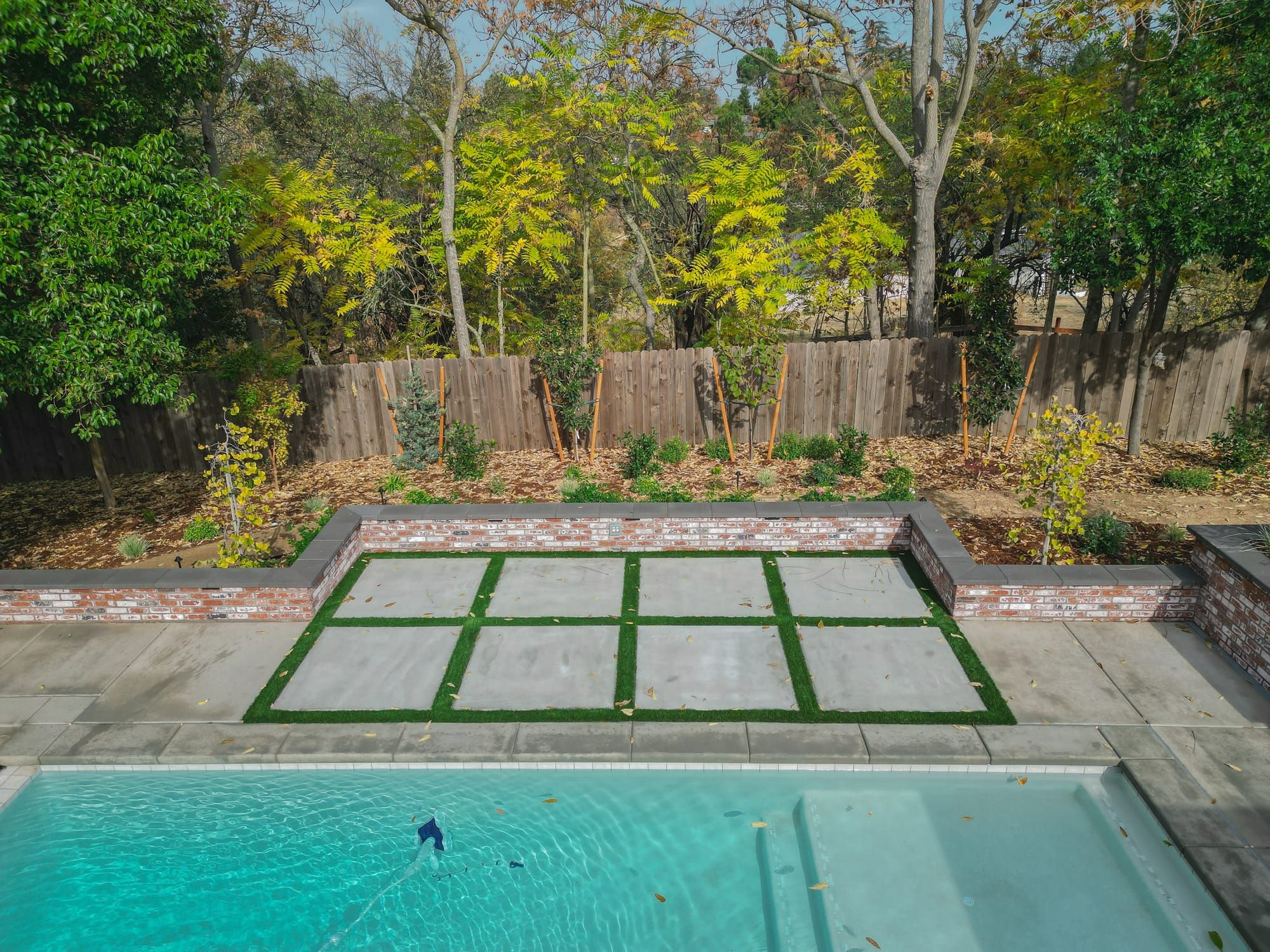 Paver patio with turf inlay, brick retaining wall, and pool in Sacramento
